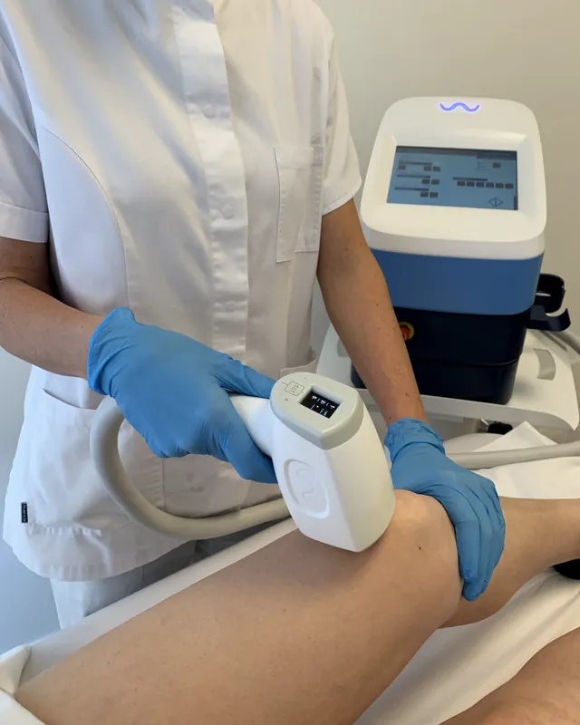 Il manipolo del laser a diodo sulla gamba, tenuto con i guanti blu, e l'apparecchio con lo schermo acceso